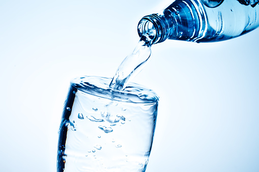 Fresh drinking water is poured in a glass. Blue background.